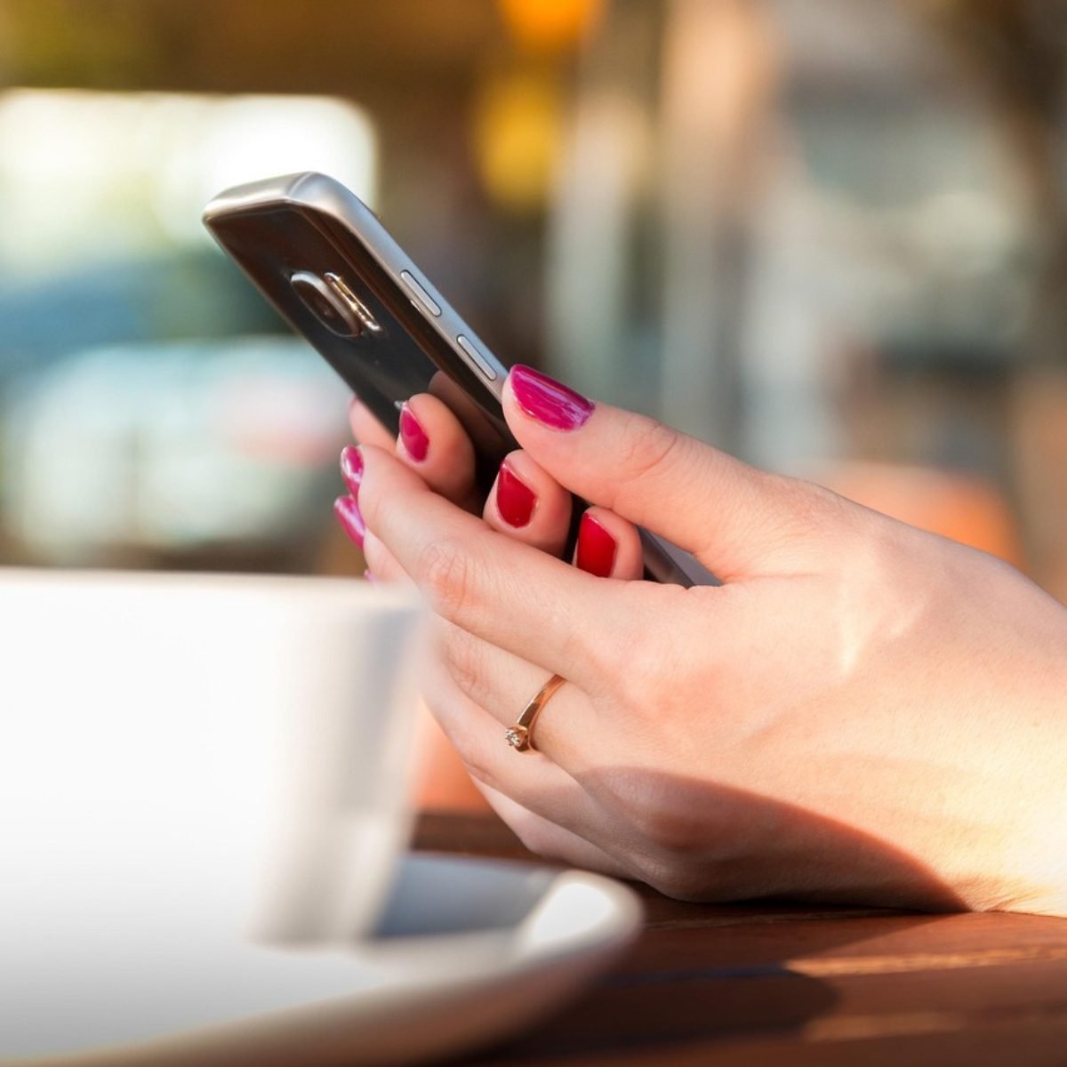 Woman holding a phone with pink nails, sending a message to her long distance partner.